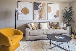 A living room with a sofa, a yellow armchair, a coffee table, and three abstract paintings on the wall. - Luxury Two Bedroom Condo - Heart of Town Center (Big Sky)