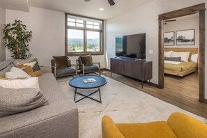 Una sala de estar moderna con un sofá, sillones, una mesa de centro, un televisor y una cama con cabecera de madera.