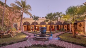 A courtyard with a central fountain, palm trees, and a building with arched windows. - Hotel Plaza del Fuerte by Balderrama Hotel Collection  (El Fuerte)