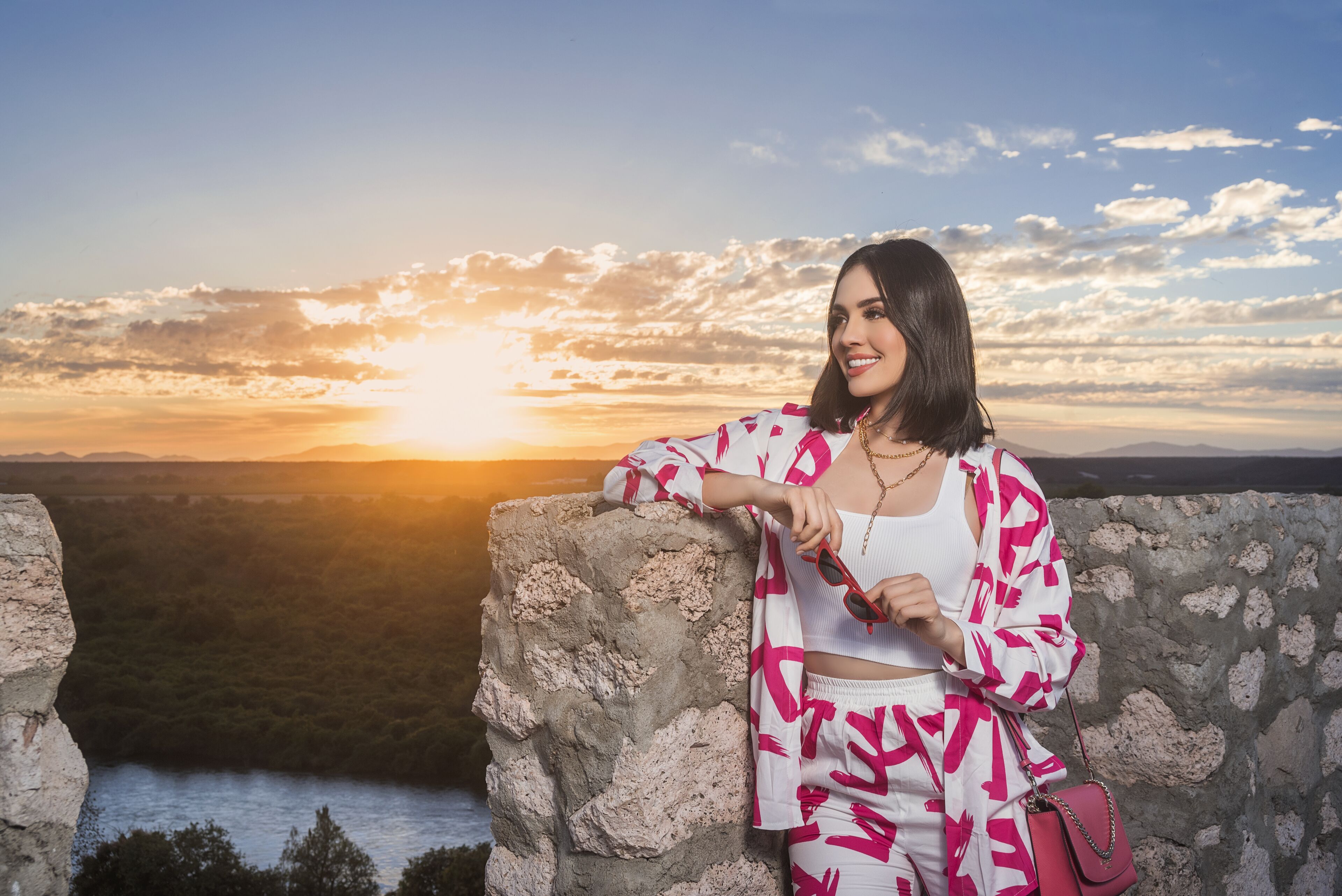 A person leaning on a stone wall with a scenic view of a sunset over a valley.