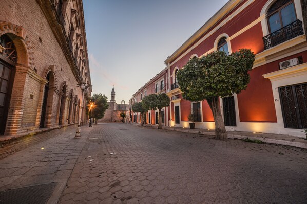 A cobblestone street lined with historic buildings, featuring brick facades, arched doorways, and traditional balconies.
