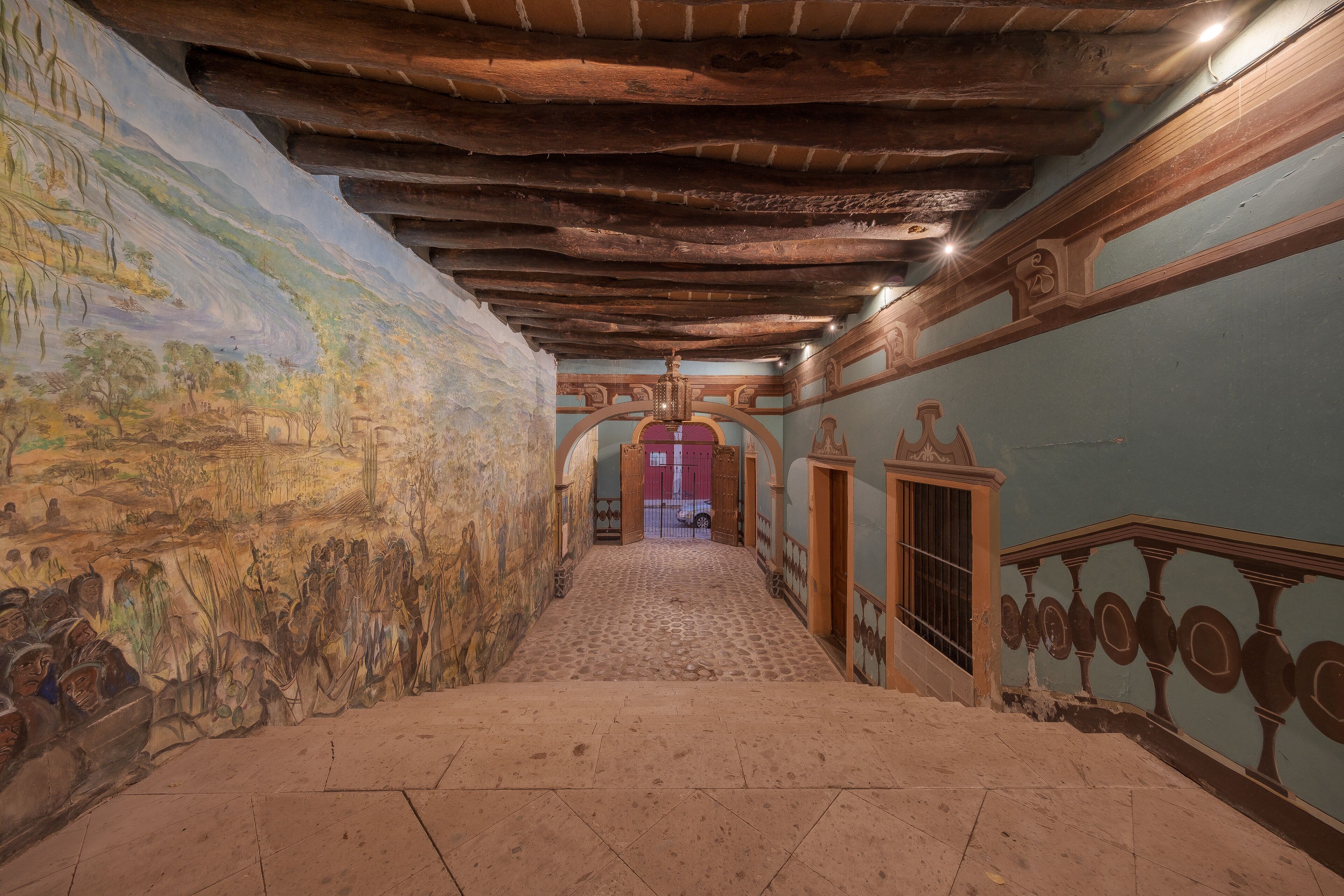Un pasillo con suelo de baldosas, un mural en la pared izquierda y techo de madera.