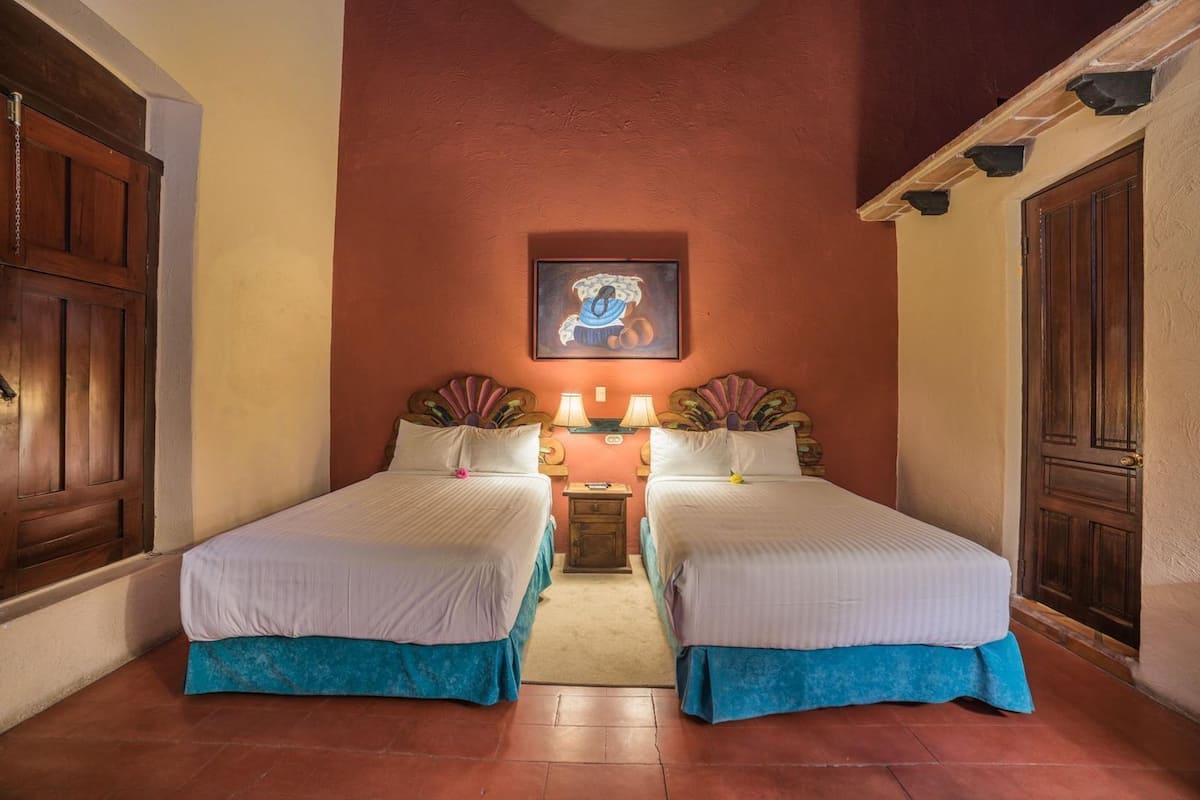 Una habitación con dos camas, un cuadro en la pared y una mesita de noche con lámparas.