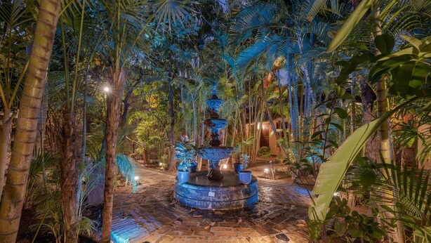 A circular water fountain surrounded by palm trees and illuminated by soft lighting. - Hotel Plaza del Fuerte by Balderrama Hotel Collection  (El Fuerte)
