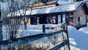 A modern wooden cabin with a large porch, surrounded by snow-covered ground and trees. - Your Cozy Home in the Woods (Soldotna)