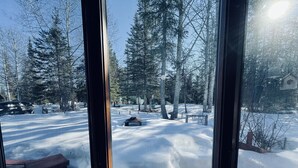 A view through a window of a snowy landscape with trees, a bench, and a car. - Your Cozy Home in the Woods (Soldotna)