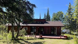 A wooden cabin with a porch, surrounded by trees and a clear sky. - Your Cozy Home in the Woods (Soldotna)
