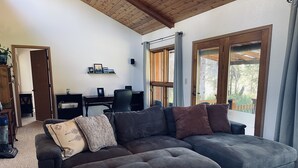 A living room with a sectional sofa, a desk, and a view of the outdoors. - Your Cozy Home in the Woods (Soldotna)