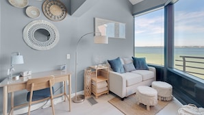 Una sala de estar moderna con vistas al mar, que incluye un sofá blanco, un escritorio y decoración en la pared.