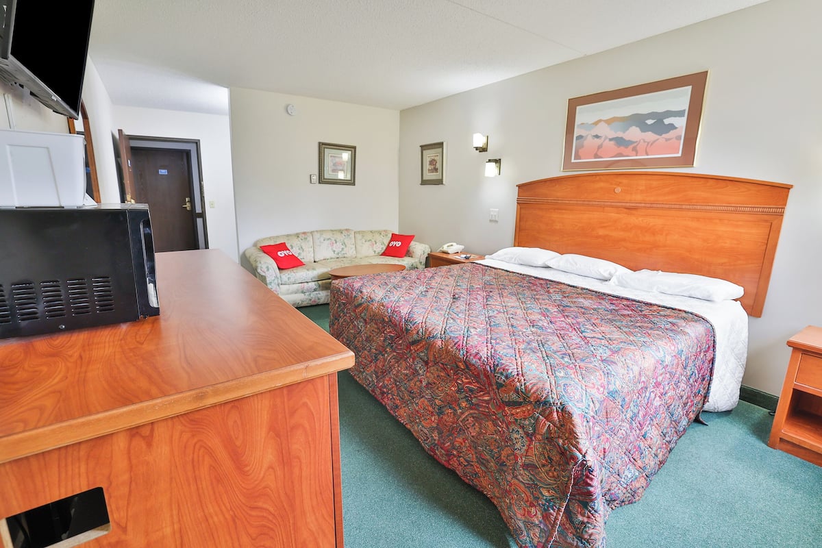 Una habitación de hotel con un escritorio de madera, una cama con colcha estampada, un sofá floral y un cuadro en la pared.