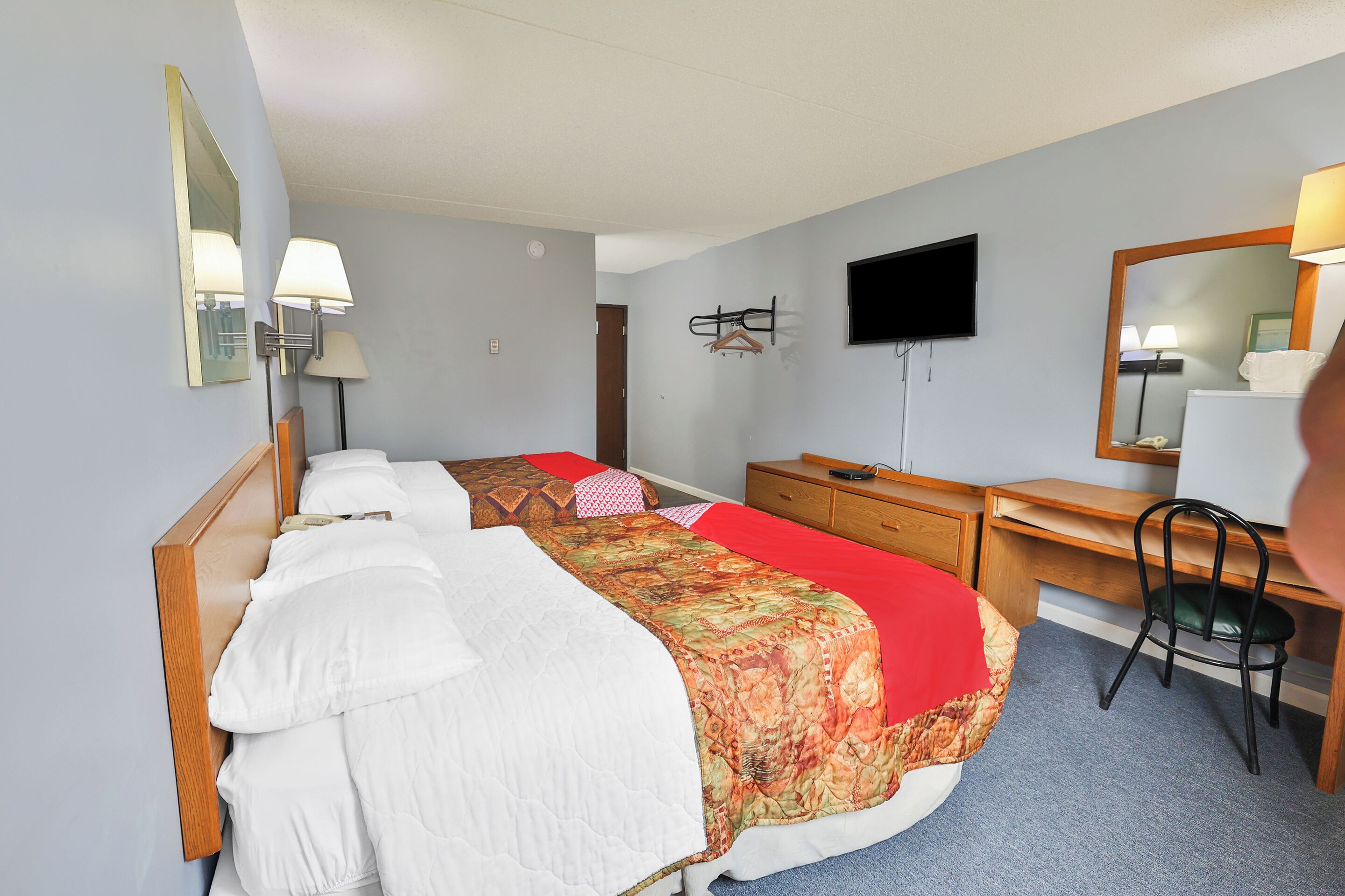 A hotel room with two beds, a desk, a chair, a TV, and a mirror.