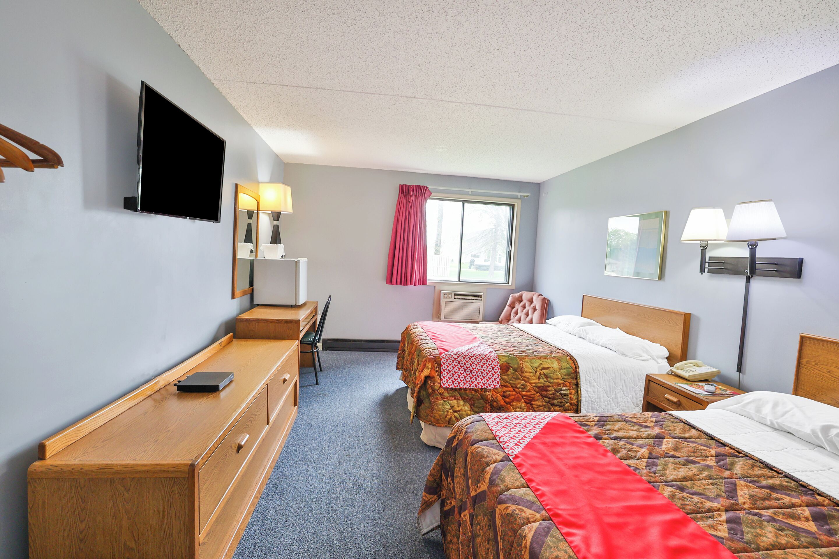 A hotel room with two beds, a desk, a chair, a TV, and a window with curtains.