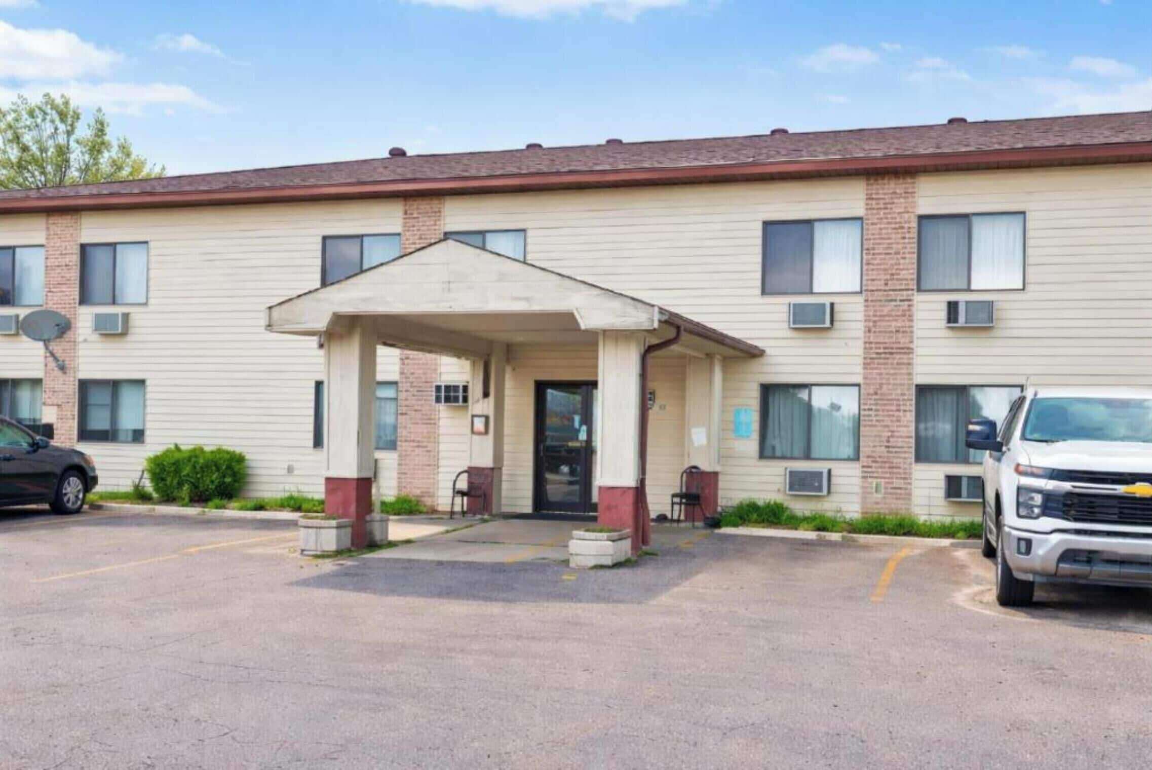 A two-story motel with a covered entrance, a parking lot, and a white pickup truck parked in front.
