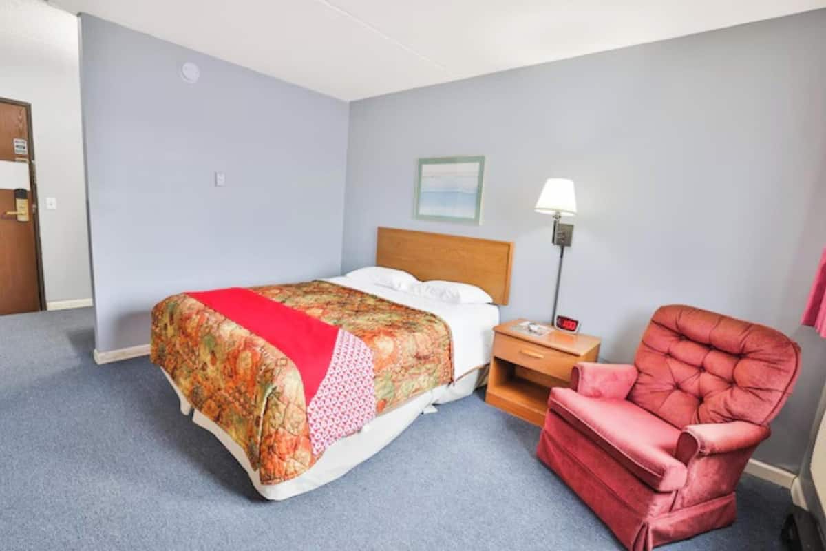 Una habitación de hotel con una cama, una mesita de noche, una lámpara y un sillón rojo.