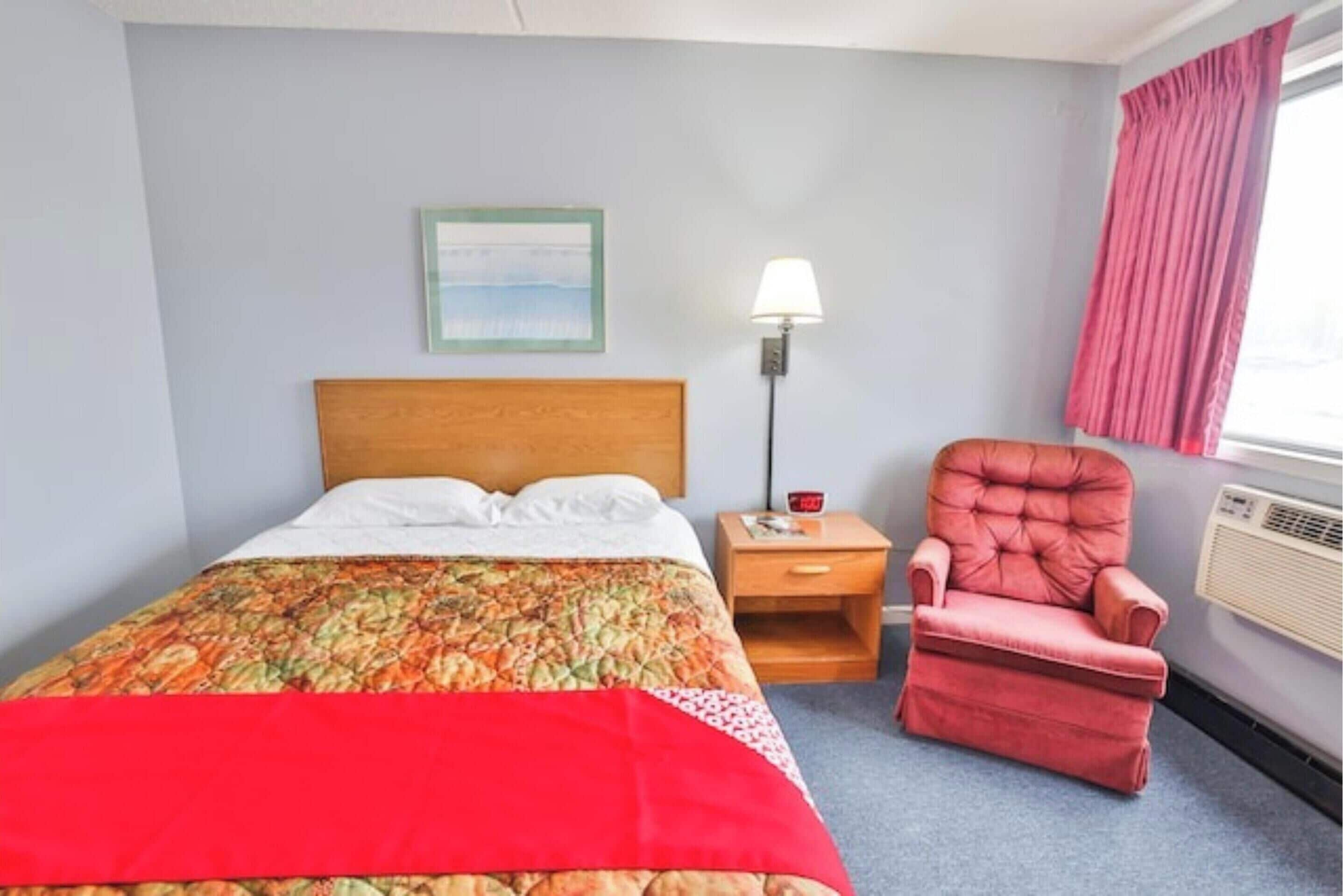 A hotel room with a bed, a nightstand, a chair, a lamp, and a window with curtains.