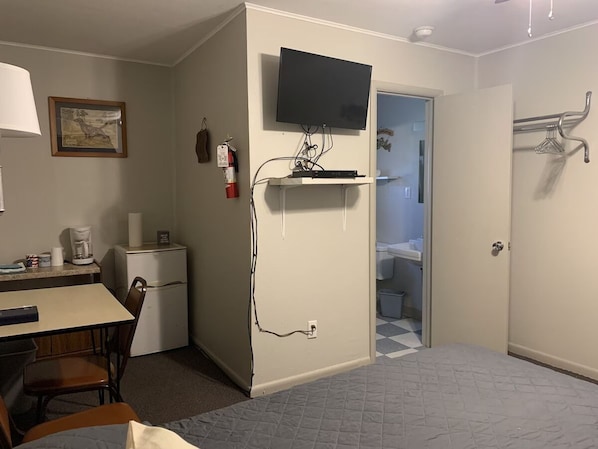 A hotel room with a desk, chair, television, and a small kitchenette.