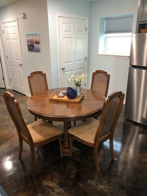 A dining area with a round wooden table, four wooden chairs, and a tray with a pitcher, teapot, and vase of flowers.
