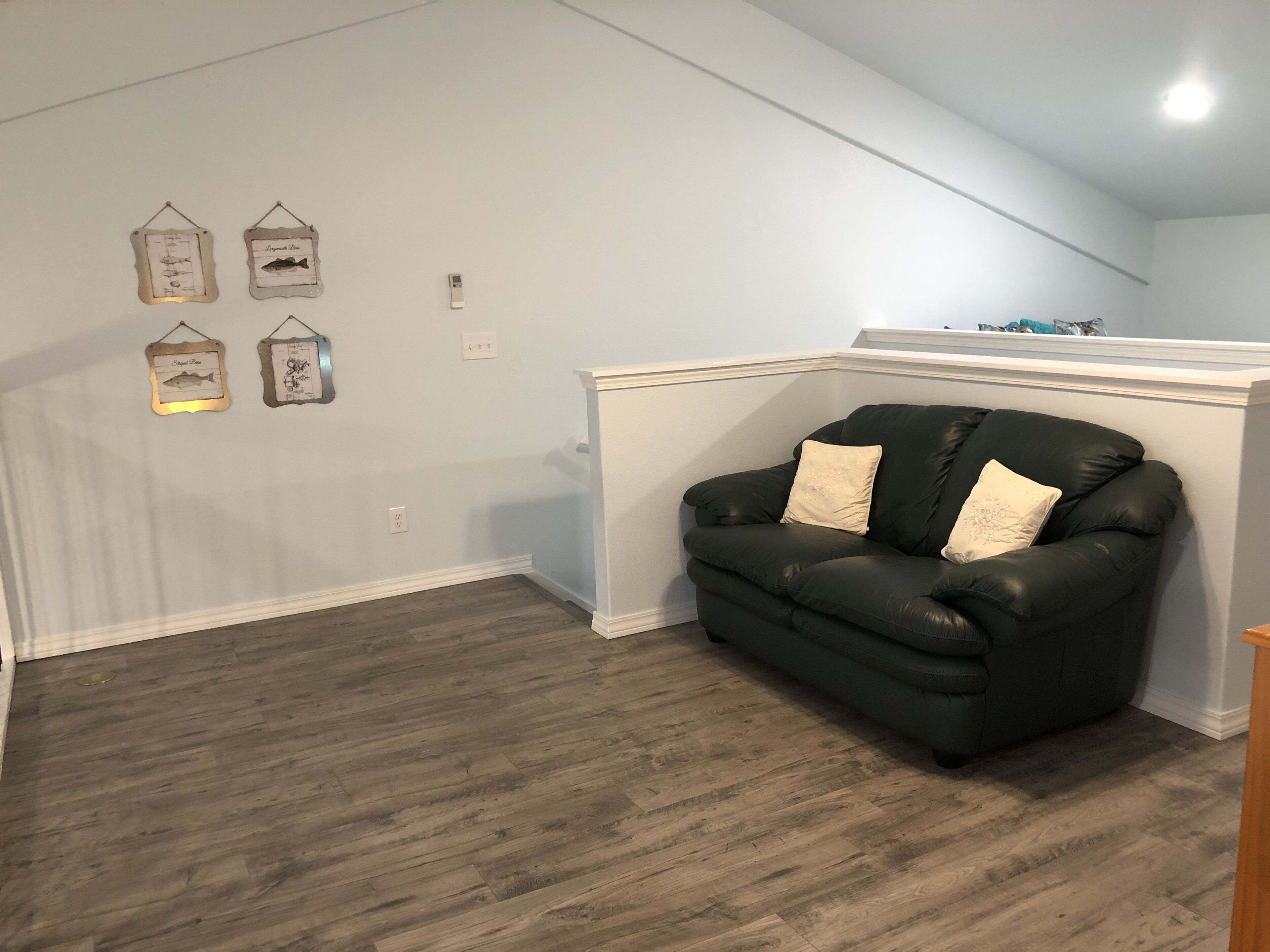 Ein Zimmer mit einer schwarzen Ledersofa, hellblauen Wänden und Holzdielen.