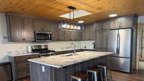 A kitchen with wooden cabinets, a stainless steel refrigerator, a built-in microwave, a gas stove, and a large island with stools.