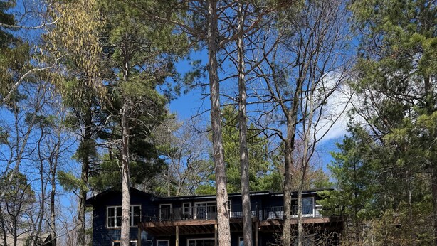 A house with a deck, a stone pathway, and a dock leading to a body of water.