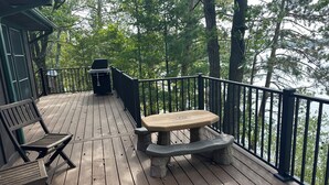 A wooden deck with a picnic table and benches, surrounded by a railing, overlooking a forested area.