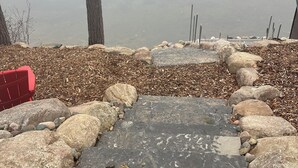 A stone patio with a red bench, surrounded by rocks and pebbles, overlooking a body of water.