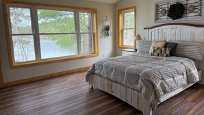A bedroom with a large window, a bed with multiple pillows, and a headboard with a decorative wreath.
