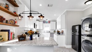 Una cocina moderna con armarios blancos, encimera de granito y lavadora secadora integrada.