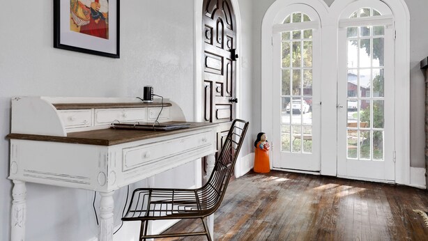 Una habitación con un escritorio blanco, una silla y dos puertas blancas en arco con paneles de vidrio.