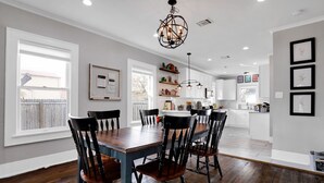 Un comedor con mesa y sillas de madera, una araña y una cocina al fondo.