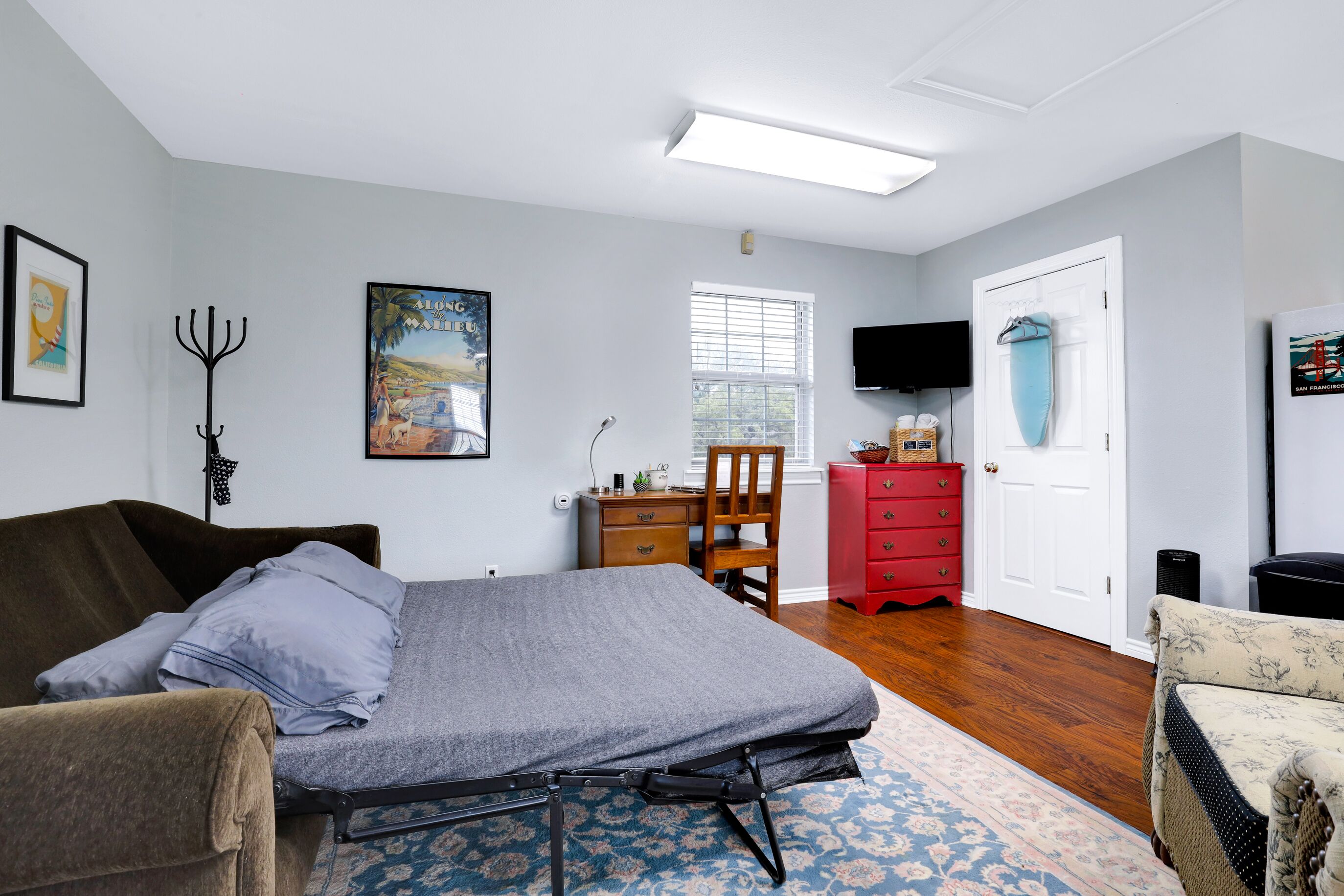 A bedroom with a bed, a desk, a chair, a dresser, and a television.
