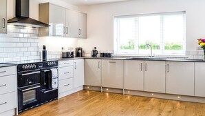 A modern kitchen with white cabinets, a black stove, and a window with blinds. - 4 bedroom accommodation in Carlisle (Carlisle)