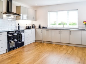 A modern kitchen with white cabinets, a black stove, and a window with blinds.