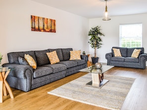Ein Wohnzimmer mit zwei grauen Sofas, einem Glastisch, einer Topfpflanze und einem Gemälde an der Wand.