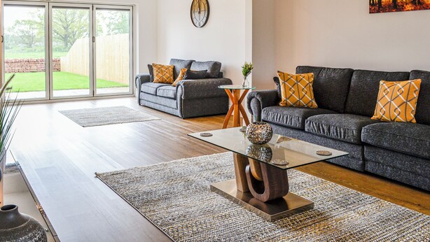 A modern living room with a glass coffee table, two sofas, a rug, and a painting on the wall. - 4 bedroom accommodation in Carlisle (Carlisle)