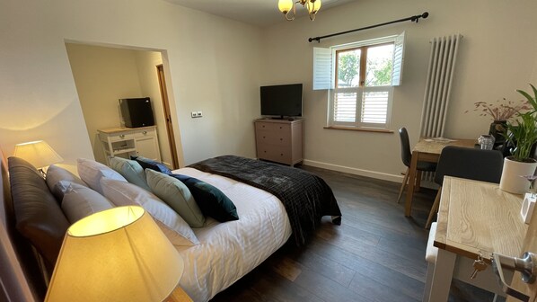 A bedroom with a bed, a desk, a chair, a TV, a lamp, a window with blinds, and a radiator. - Moorview House (Bideford)