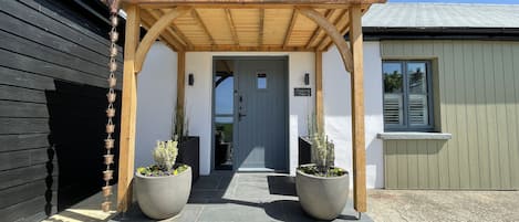A wooden pergola entrance with a grey door, two large planters with flowers, and a sign reading "Moorview House".