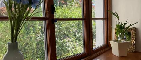 A window with a view of greenery and a vase with flowers on a wooden ledge.
