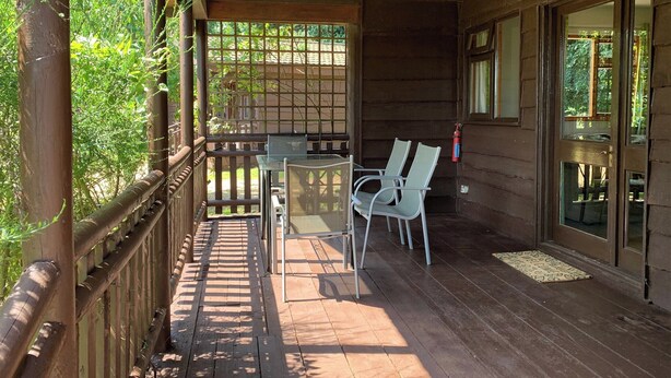 A wooden deck with a table and chairs, a fire extinguisher, and a view of greenery. - Chestnut Lodge - UK38194 (Bromham)