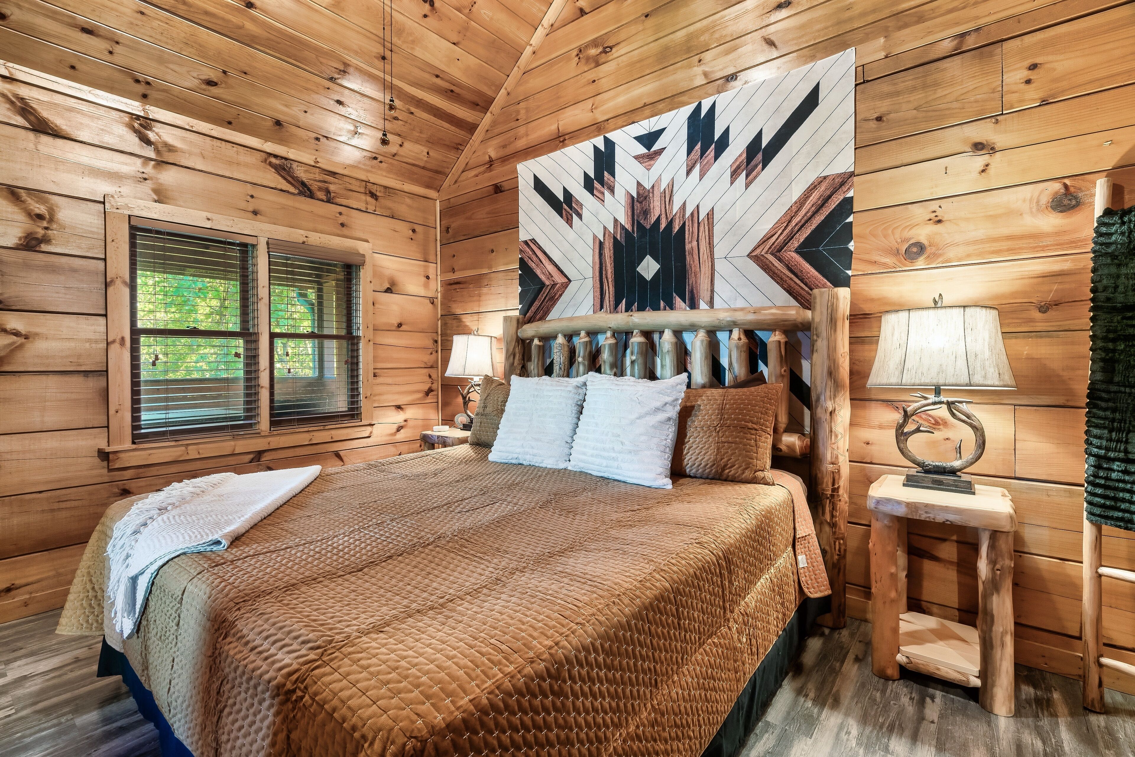 Une chambre à coucher dans une cabane en bois, avec un grand lit, une fenêtre avec des stores, une tapisserie murale et une petite table de chevet avec une lampe.
