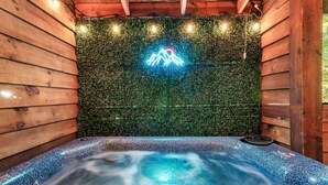 Une cabane en bois avec un jacuzzi, un panneau lumineux en forme de montagne et des guirlandes lumineuses.
