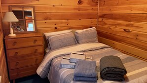 A wooden-paneled room with a bed, a nightstand, a lamp, and a mirror.