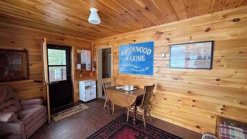 A cozy cabin interior with a wooden ceiling, a dining table with chairs, a sofa, and a sign reading 'Brookwood Marine.'