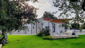 Un bâtiment blanc surmonté d’un toit recouvert de tuiles rouges, doté d’un espace extérieur aménagé avec des sièges et d’une pelouse verdoyante bien entretenue.