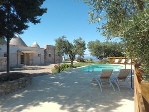 A pool area with lounge chairs, a stone building, and a view of the sea. - Panoramic trulli for 7 people in the hills with a private pool, 8 km from the sea (Monopoli)