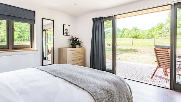 A bedroom with a bed, a dresser, a mirror, and a view of an outdoor patio. - 1 bedroom accommodation in Chiddingstone (Chiddingstone)