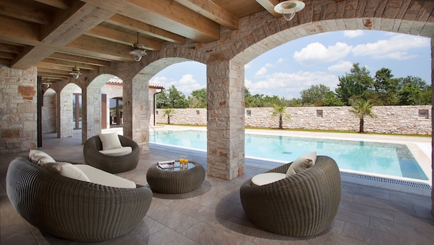 Un’area esterna coperta con colonne in pietra, mobili in vimini e una piscina.