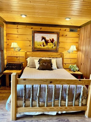 A wooden room with a bed, two bedside tables, a painting, and a window with blinds. - Big South Fork! Peaceful, Relaxing, On the Trails…Six Decks ~ Nature’s Paradise! (Strunk)
