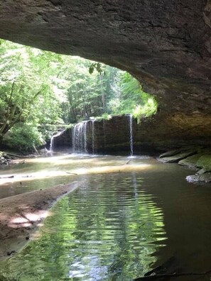 A natural cave entrance with a waterfall and a calm pool of water reflecting the surrounding greenery. - Big South Fork! Peaceful, Relaxing, On the Trails…Six Decks ~ Nature’s Paradise! (Strunk)