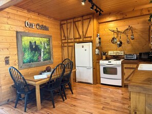 A cabin interior with a dining table, chairs, a refrigerator, a stove, and a microwave. - Big South Fork! Peaceful, Relaxing, On the Trails…Six Decks ~ Nature’s Paradise! (Strunk)